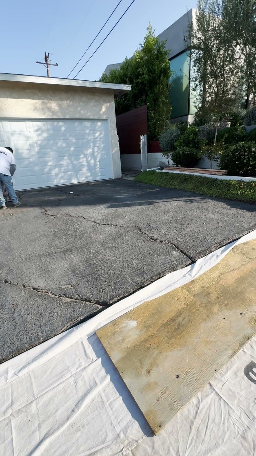 Cracked asphalt driveway in front of a garage in Culver City before Buildda replaced it with concrete