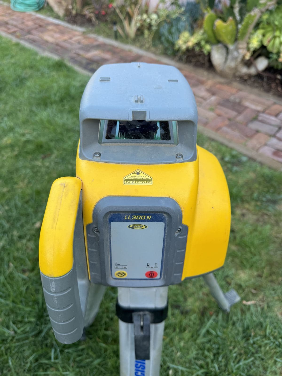Yellow DeWalt rotating laser level on tripod used by Buildda for drainage grading in Carlson Park walkway project