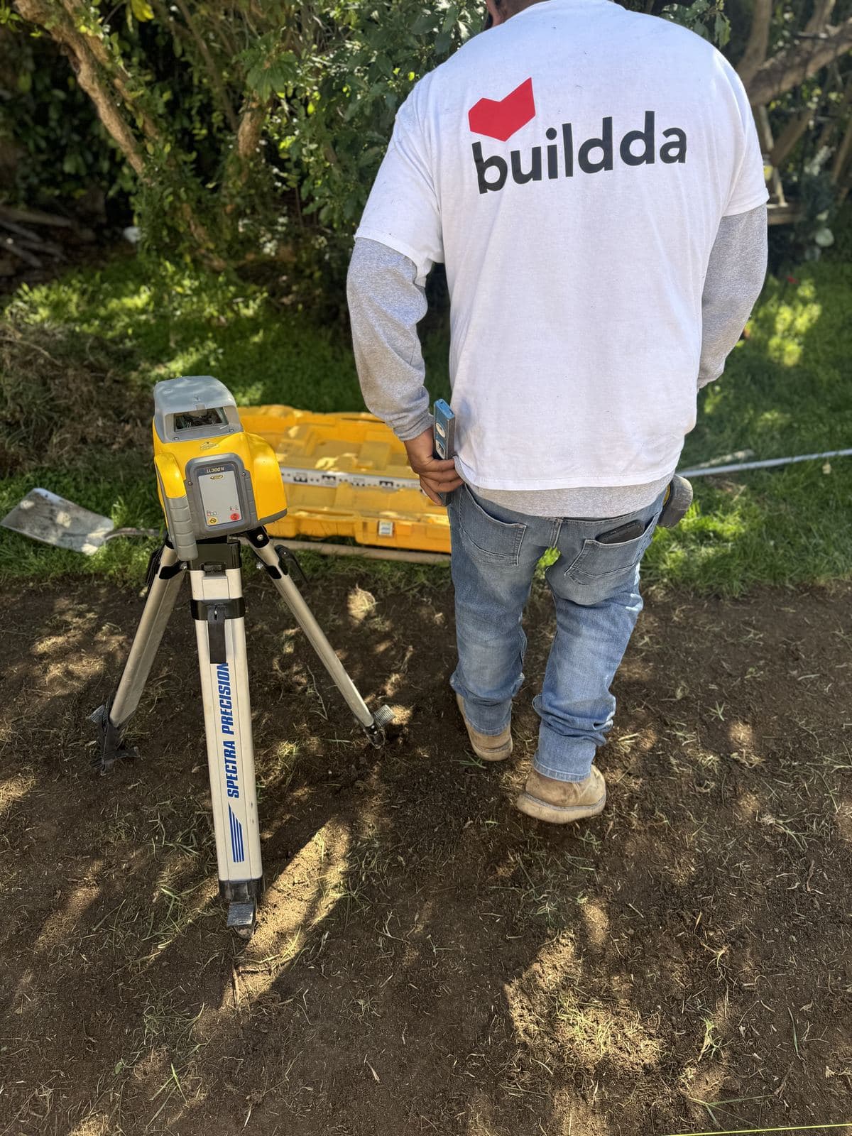 Buildda crew member in branded shirt working with laser level during Carlson Park walkway grading