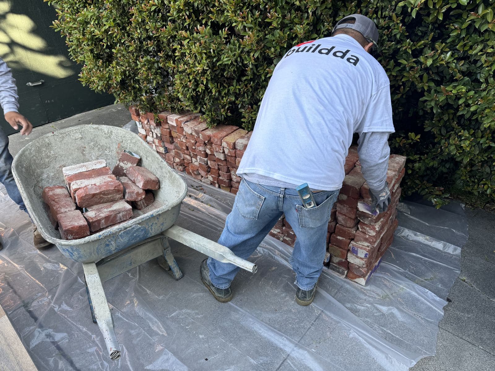 Buildda crew member in branded shirt pushing wheelbarrow of reclaimed bricks in Carlson Park backyard