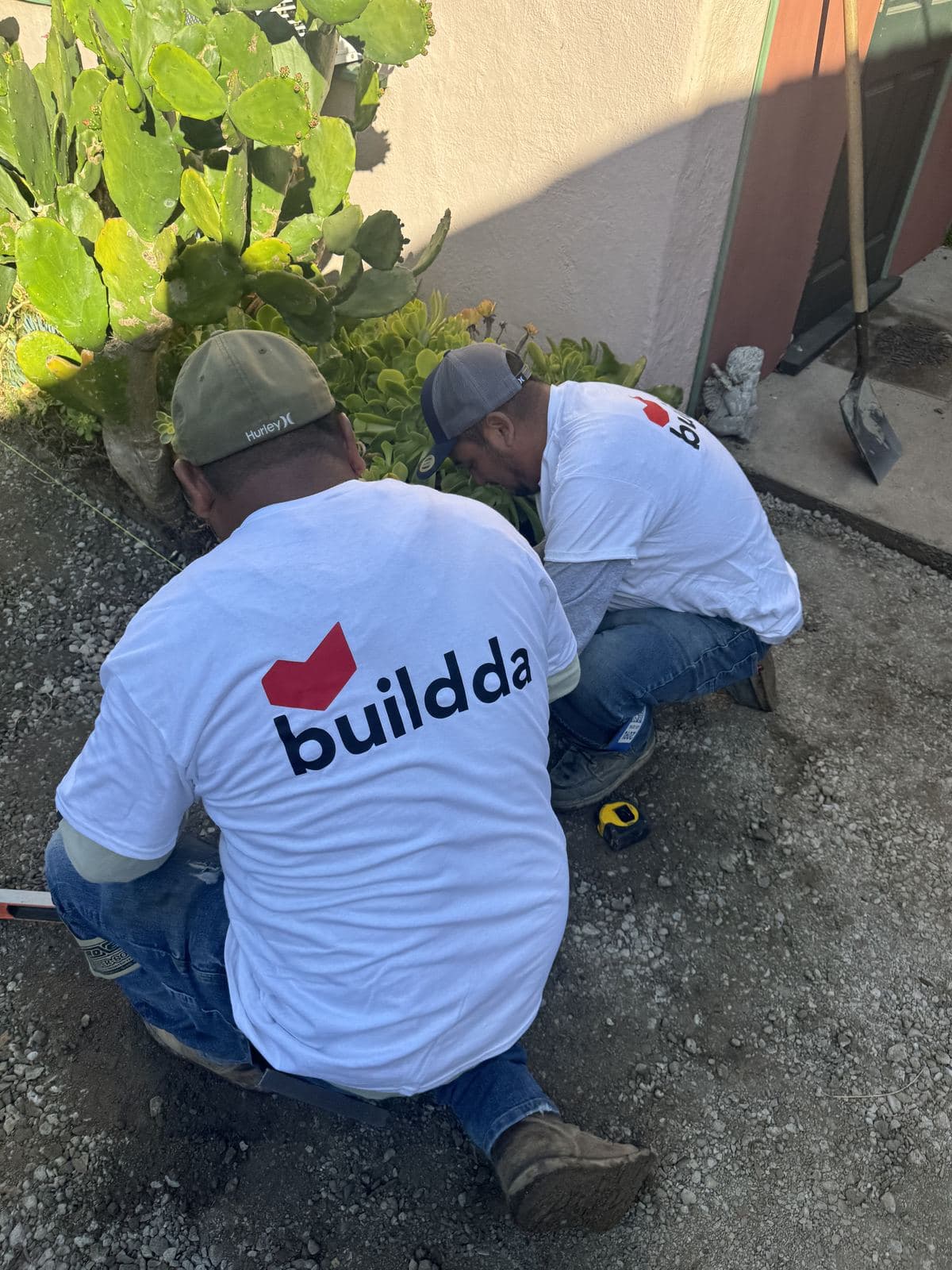 Two Buildda crew members in branded shirts relocating sprinkler heads around cacti in Carlson Park backyard