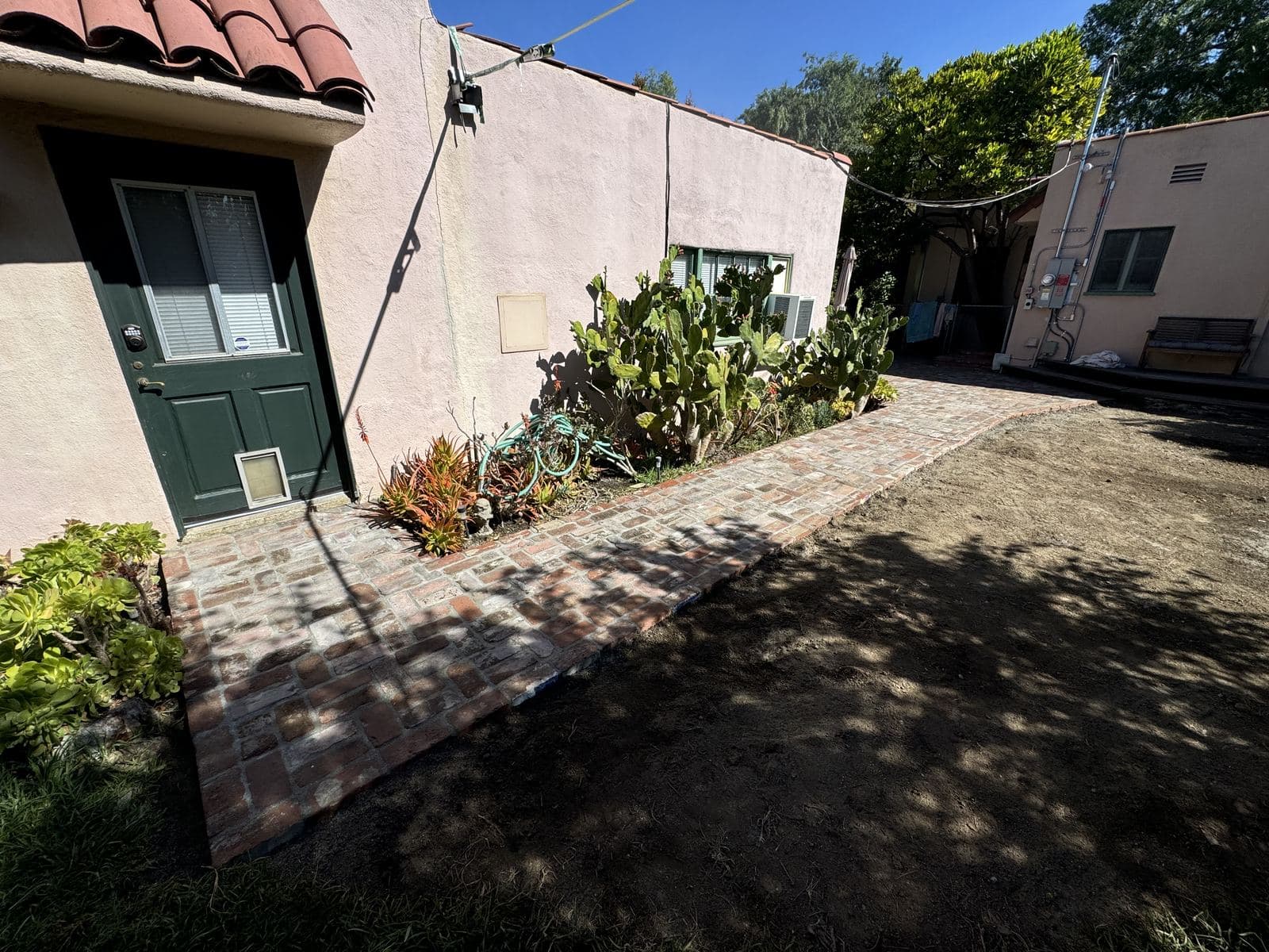 Finished reclaimed brick walkway leading to green door of Spanish-style Culver City home with cacti along side
