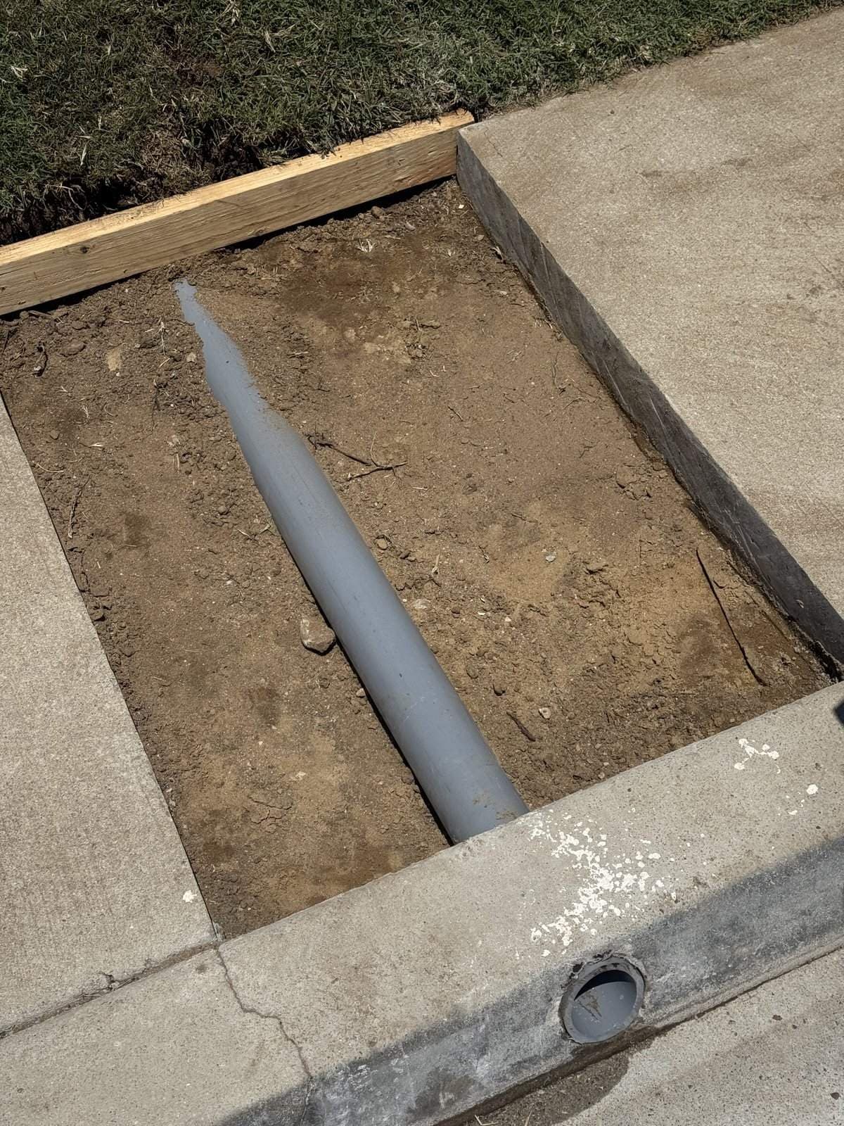 Gray drain pipe running through a cut section of sidewalk to the curb in Culver City