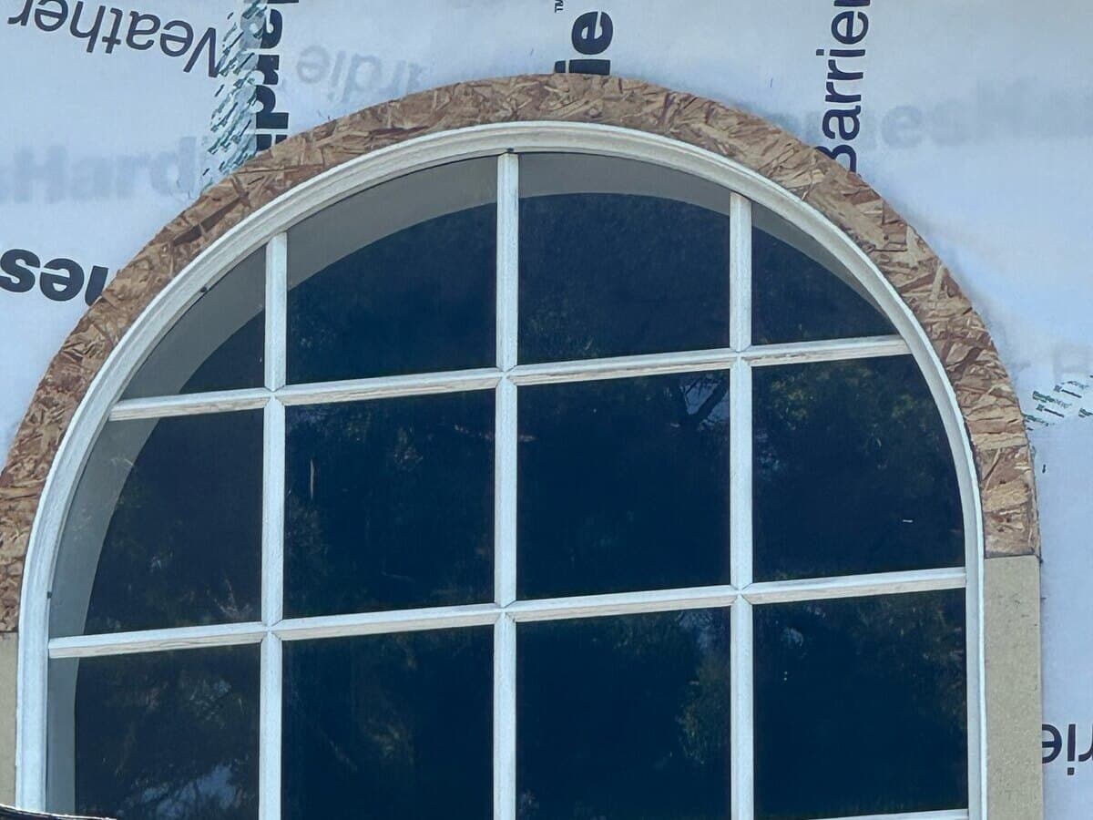Arched upstairs window surrounded by weather barrier before the new siding on a Palms home