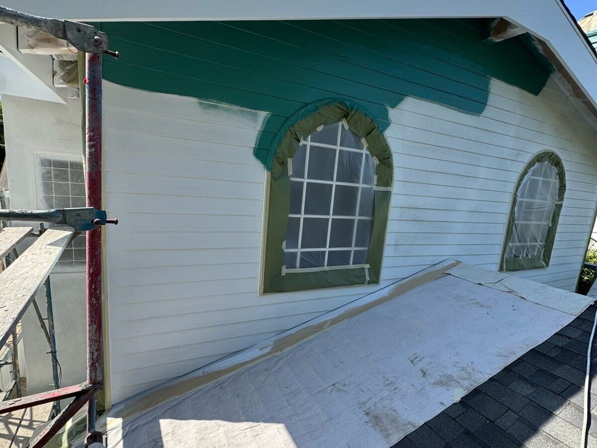 Teal paint going on over white primer at an upper gable with arched windows in Palms