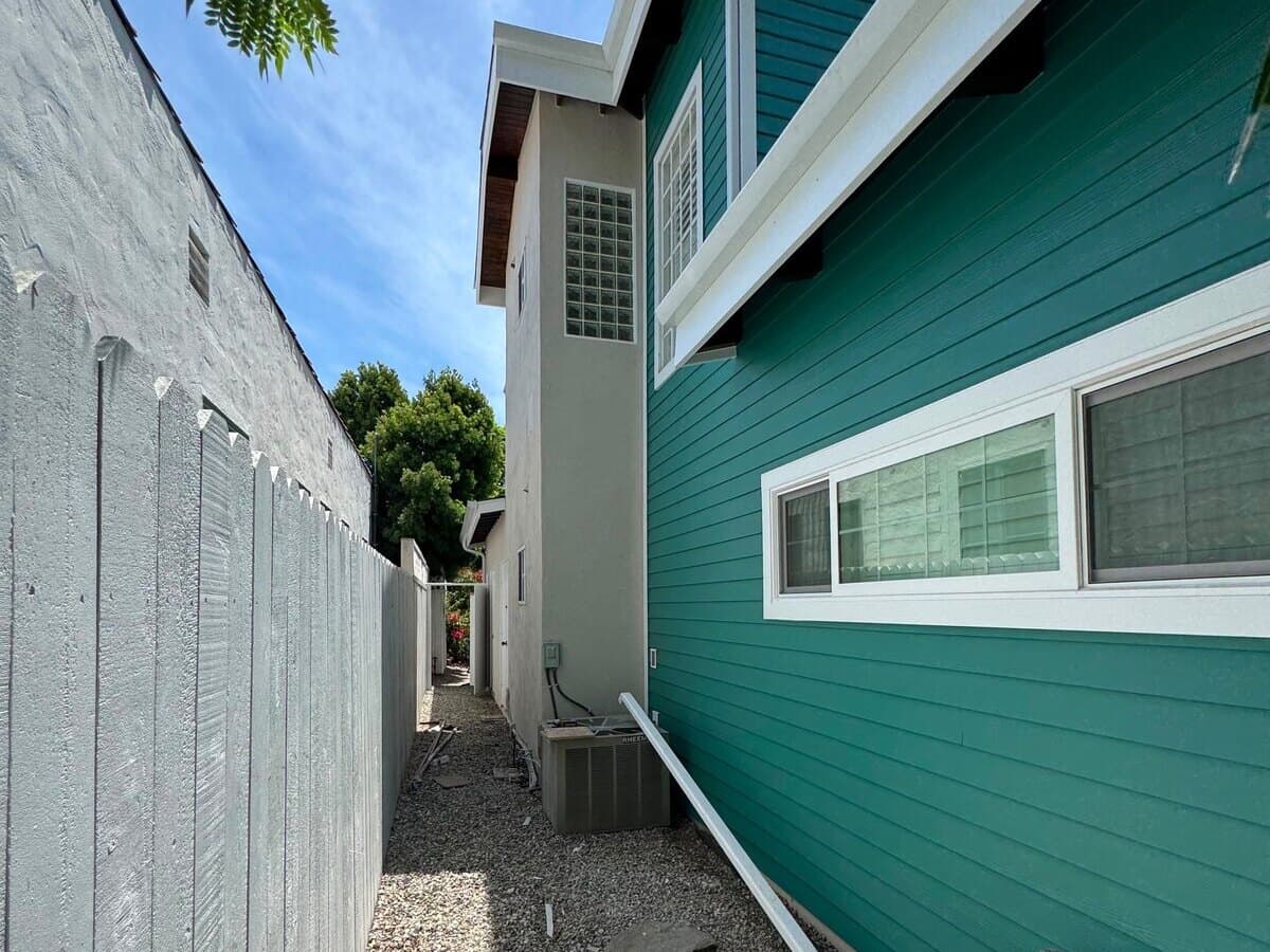 Finished side wall with new windows and teal fiber-cement siding along a side yard in Palms