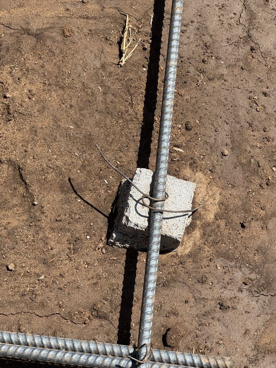 Close-up of rebar resting on a small concrete block so the steel sits inside the slab, Santa Monica driveway