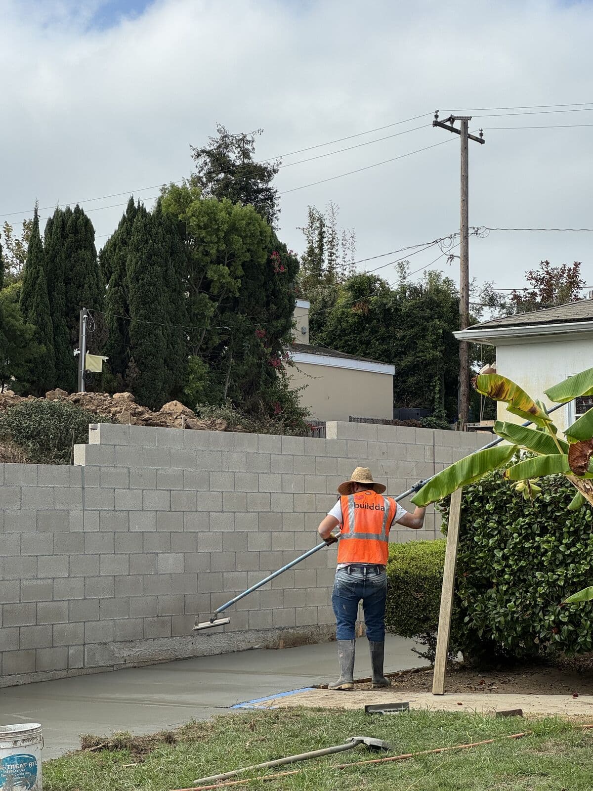 Worker screeding a fresh concrete driveway slab level along a block wall in Santa Monica